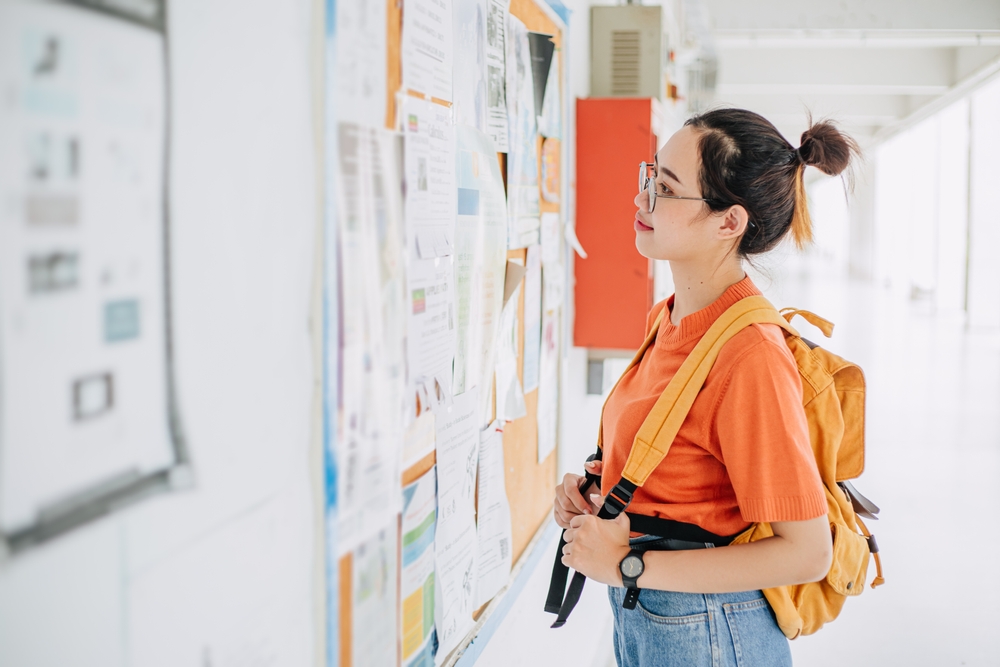 Asian university student girl looking, find search for a part time jobs, teen working during free time post announce at campus advertising billboard