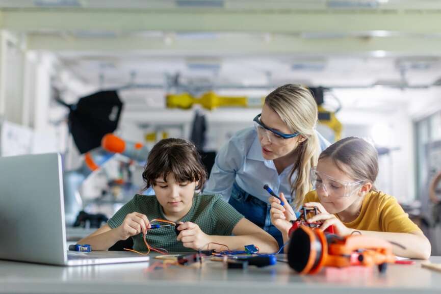 Female teacher helping to girls working on small robot, building robotic car representing the concept of Competency-Based Education to make the students skilled