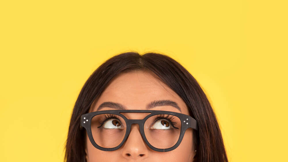 Young women with solid yellow background wearing eye glasses looking upwards