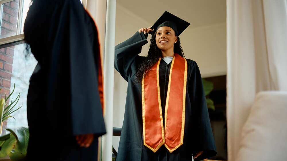 Woman looking at her in the mirror in graduation gown and hat